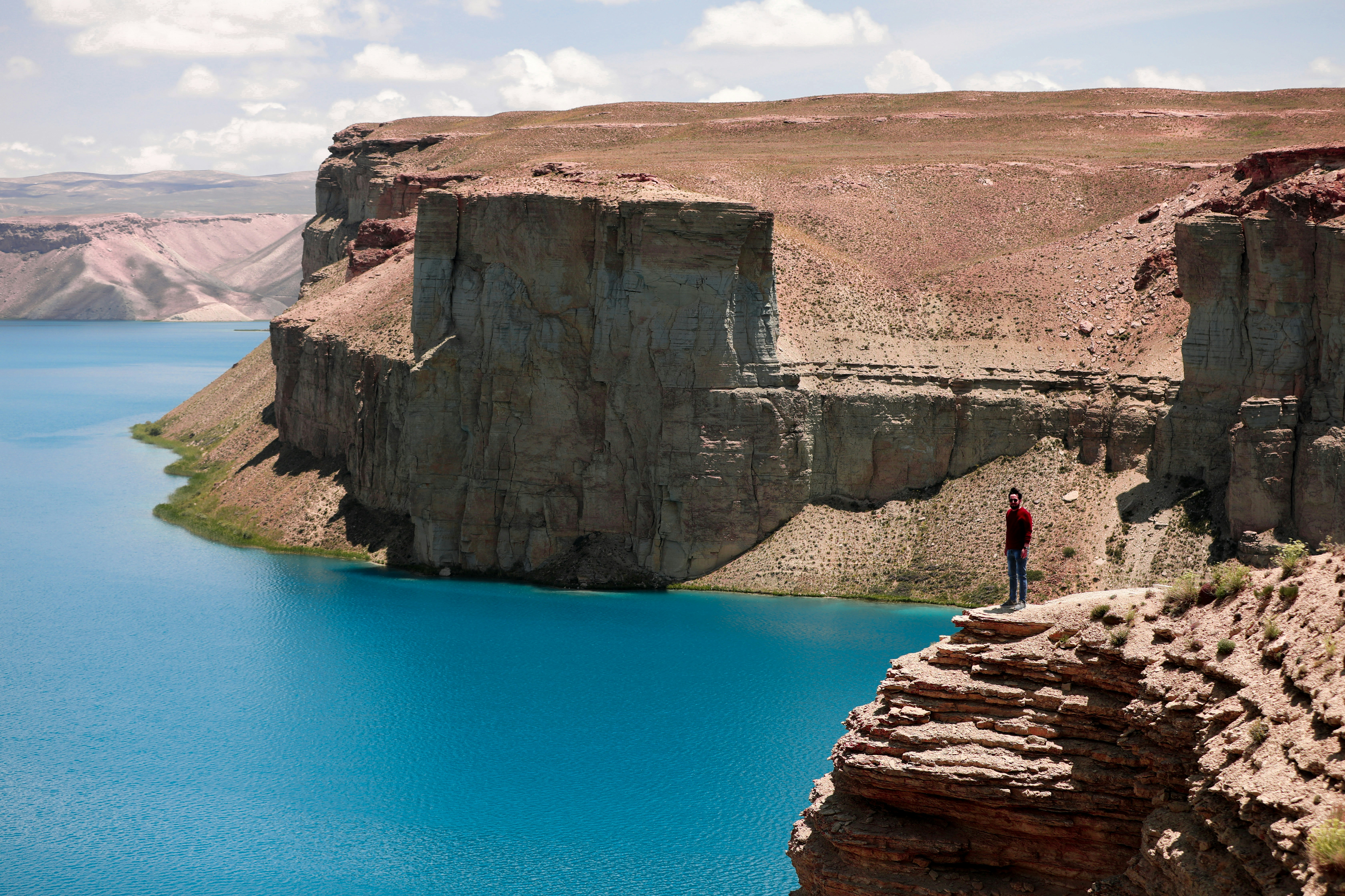 person standing on brown rock formation near blue lake during daytime afghanistan teams background