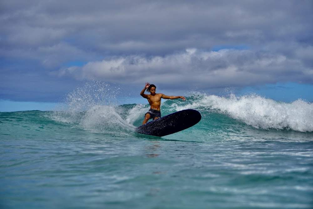 woman in black wetsuit surfing on sea waves under blue and white cloudy sky during daytime