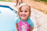 A child wearing a bright blue swimsuit and goggles, smiling by the poolside.