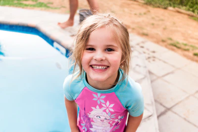 A smiling young child in colorful swim gear splashing happily in a shallow pool.
