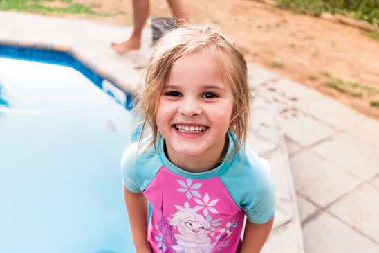A smiling instructor guiding children through a swimming lesson in a sunny outdoor pool.