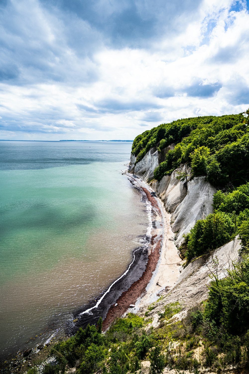 green and brown rocky mountain beside body of water under white clouds and blue sky during