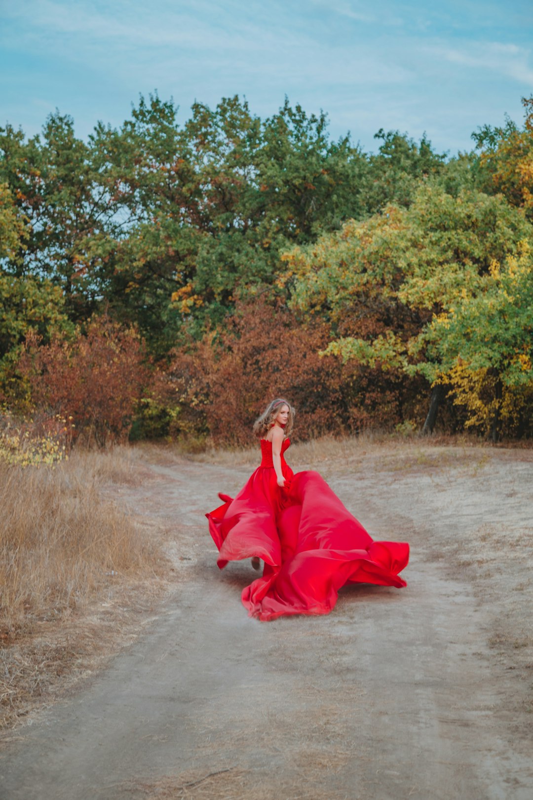 woman in red dress sitting on dirt road during daytime