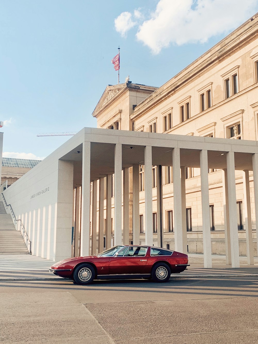 red sedan parked beside white concrete building during daytime