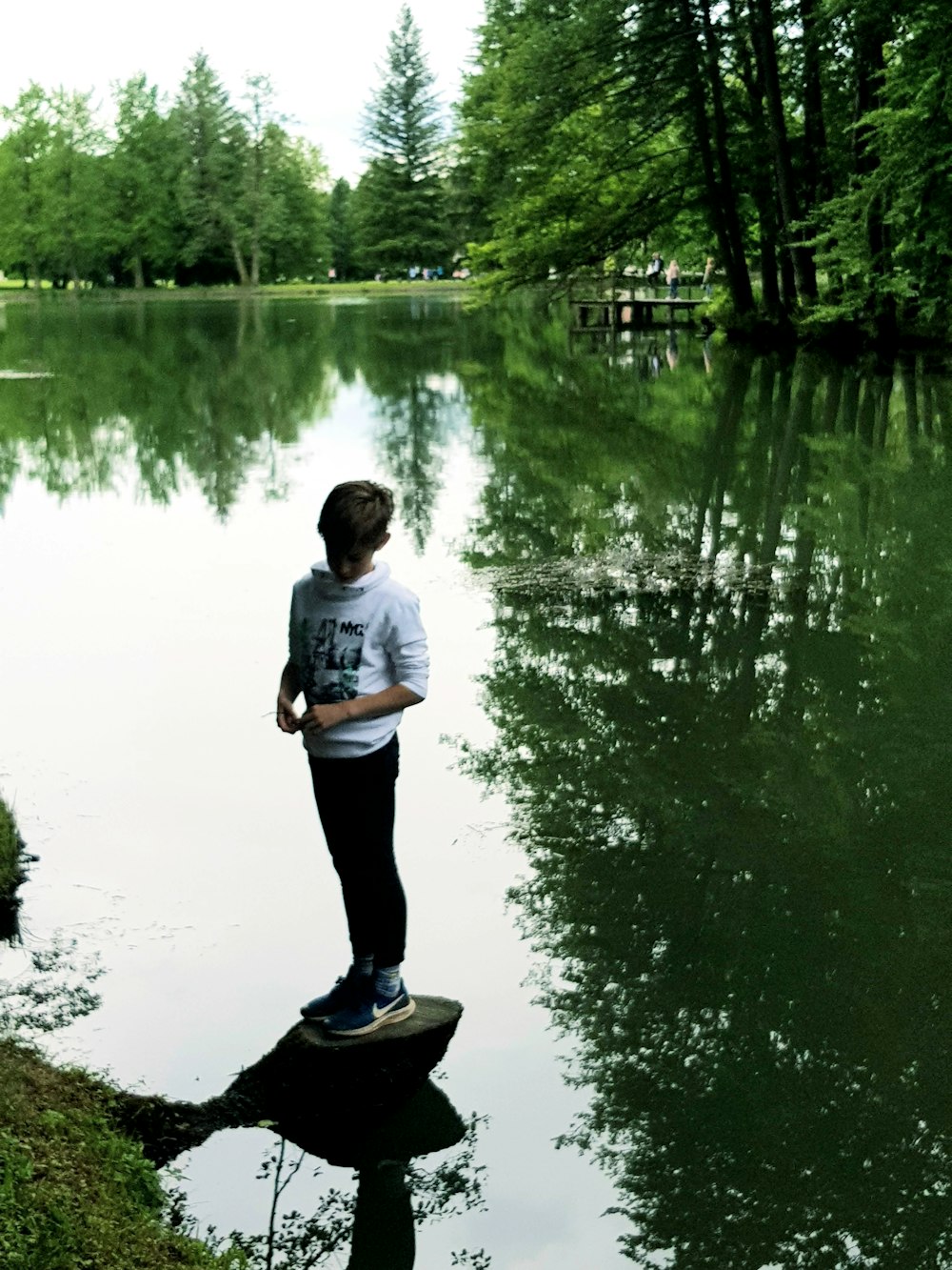 man in white shirt and black pants standing on black wooden dock during daytime