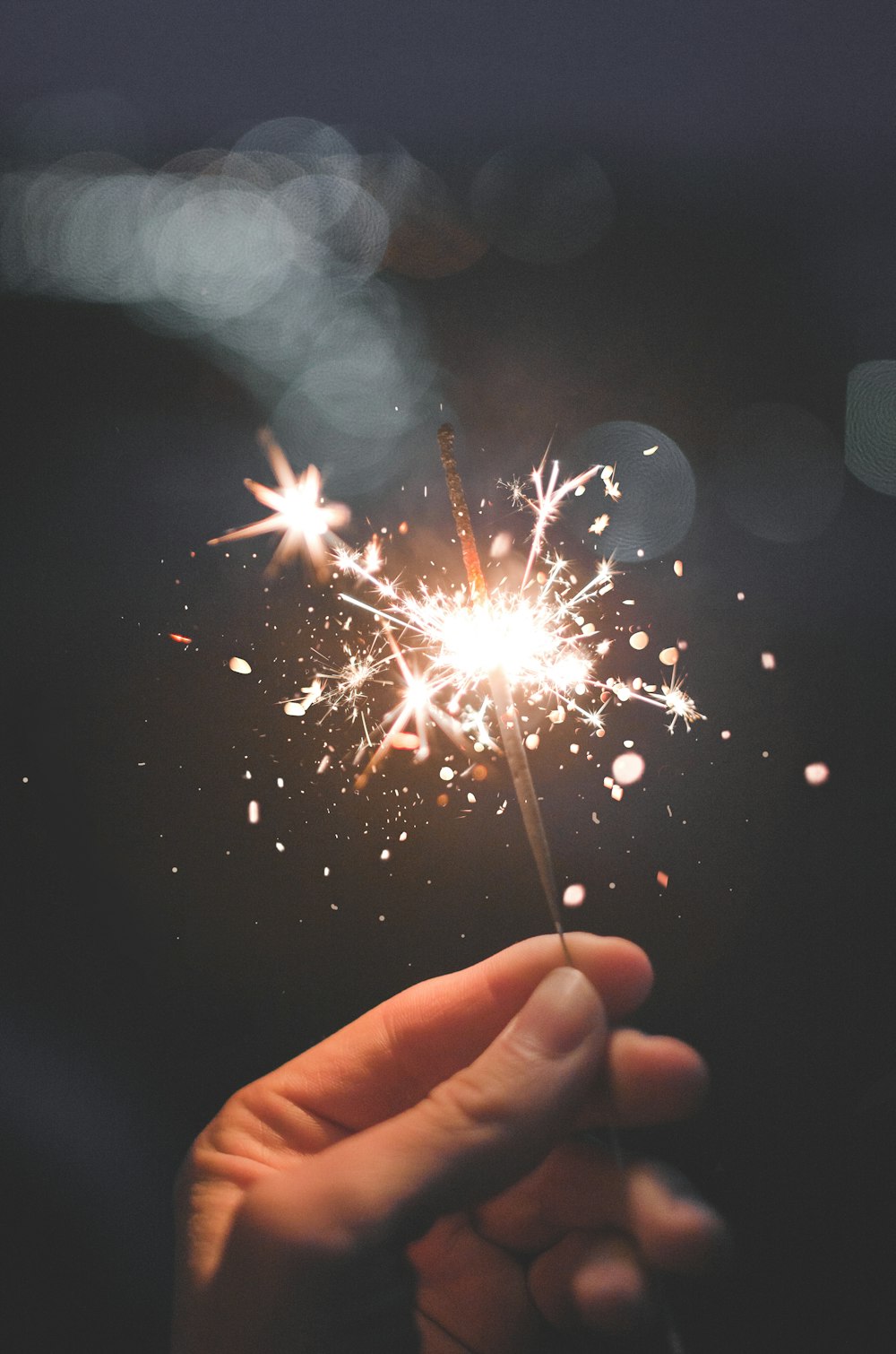 person holding lighted sparkler with white lights