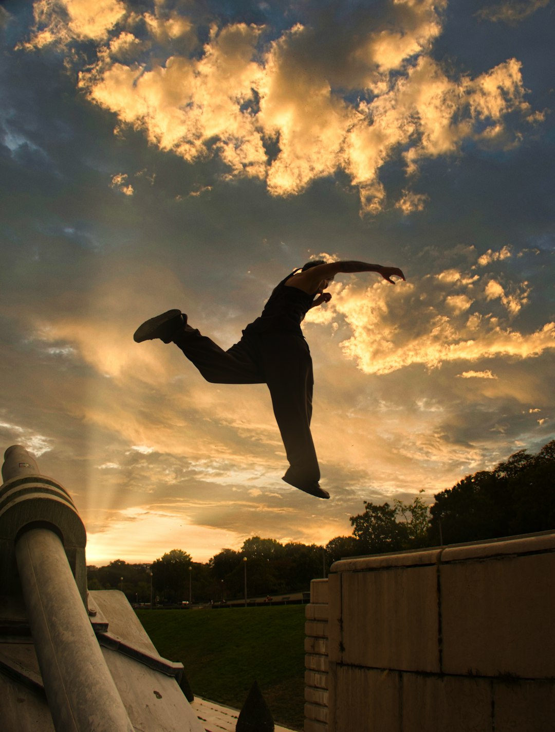 man in black jacket and pants jumping on gray concrete post under white clouds and blue