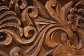 Intricate wooden carvings display detailed scrollwork and leaf motifs with smooth, flowing lines, highlighted by the natural grain and texture of the wood.