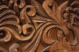 Intricate wooden carvings display detailed scrollwork and leaf motifs with smooth, flowing lines, highlighted by the natural grain and texture of the wood.