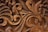 Intricate wooden carvings display detailed scrollwork and leaf motifs with smooth, flowing lines, highlighted by the natural grain and texture of the wood.