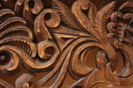 Intricate wooden carvings display detailed scrollwork and leaf motifs with smooth, flowing lines, highlighted by the natural grain and texture of the wood.