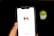 A hand holding a smartphone displaying the Gmail logo on its screen, against a dark background with a small green plant blurred in the background.