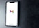 A smartphone with a white screen displays the Gmail logo, positioned on a textured dark background, with the Google branding at the bottom of the screen.