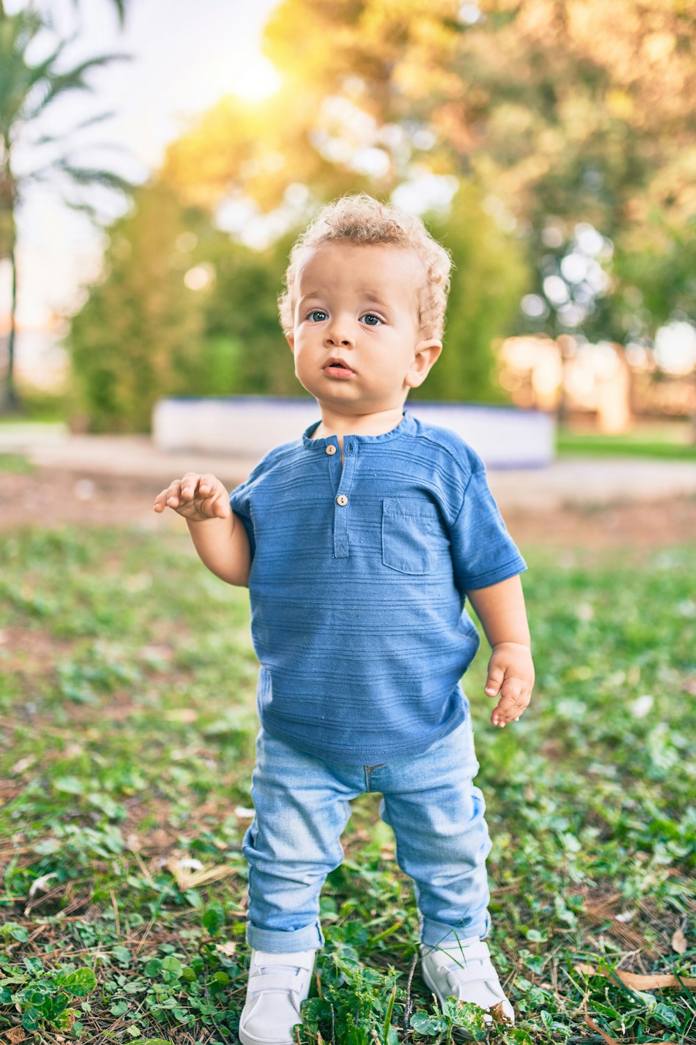 青いポロシャツと青いデニムのショートパンツを着た男の子が昼間、緑の芝生の野原に立っています