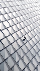 An abstract, geometric pattern created by a series of triangular glass panels arranged in a repeating diamond-shaped grid. A solitary security camera is mounted on the surface, adding an element of surveillance to the otherwise seamless architecture.