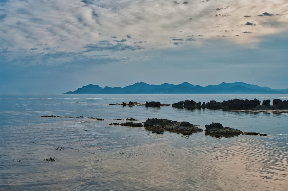 brown rocks on body of water under white clouds and blue sky during daytime