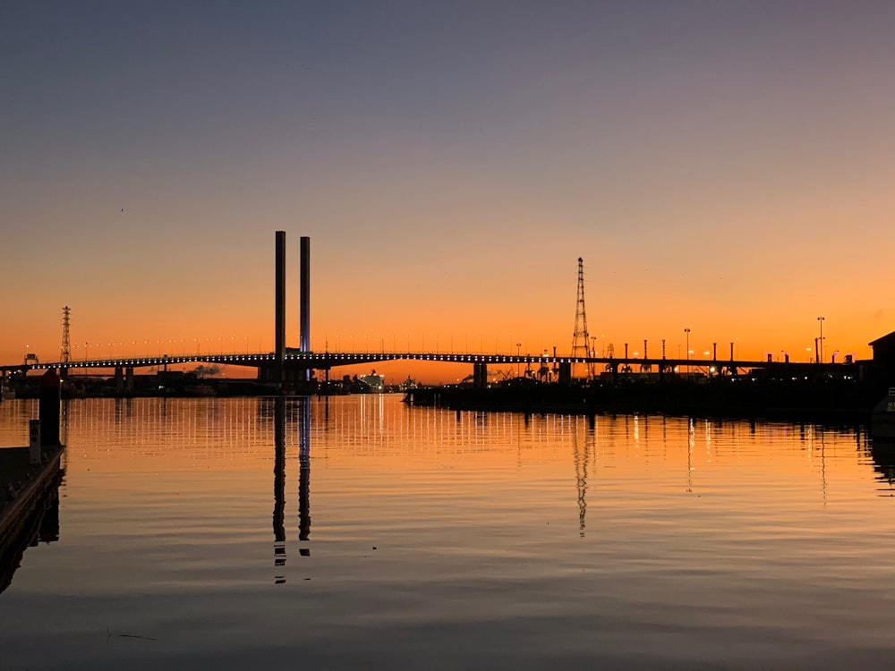 silhouette of dock on body of water during sunset