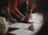 person in orange long sleeve shirt writing on white paper