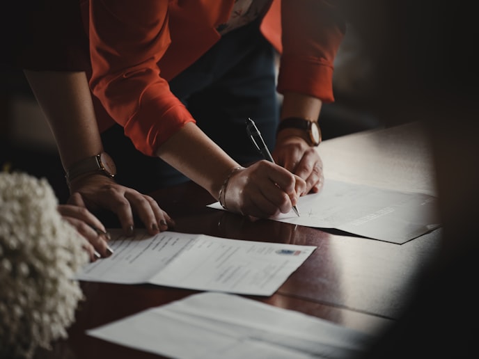 Two people's hands signing documents on dark wooden table