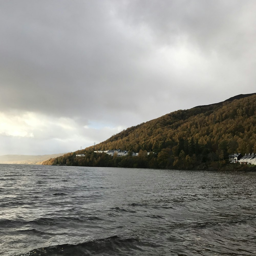 body of water near mountain under cloudy sky during daytime