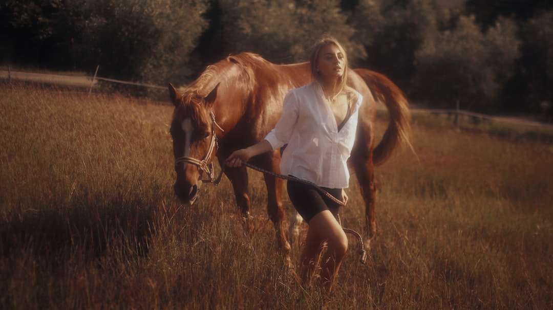 woman in white long sleeve shirt and black shorts standing beside brown horse during daytime