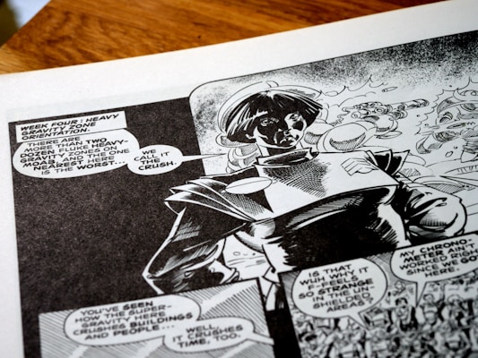 A black-and-white comic book page featuring a character wearing a futuristic or space-themed outfit. Speech bubbles contain dialogue about heavy gravity zones, adding a sci-fi narrative context. The artwork shows dynamic shading and expressive character design, capturing a sense of action and storytelling.