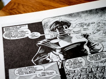 A black-and-white comic book page featuring a character wearing a futuristic or space-themed outfit. Speech bubbles contain dialogue about heavy gravity zones, adding a sci-fi narrative context. The artwork shows dynamic shading and expressive character design, capturing a sense of action and storytelling.