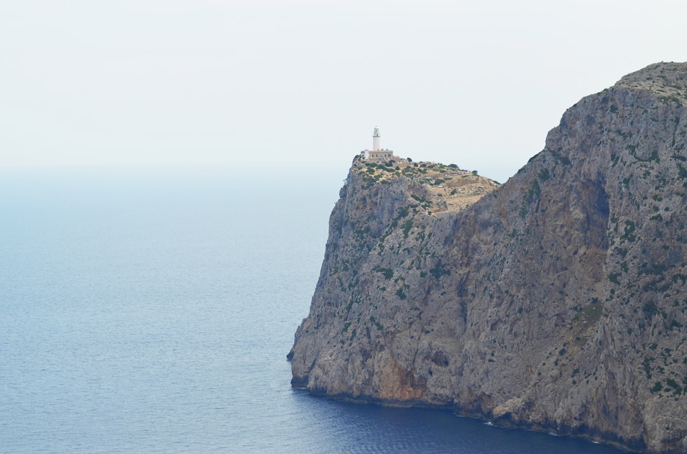 Faro blanco y marrón en una formación rocosa marrón cerca del cuerpo de agua durante el día