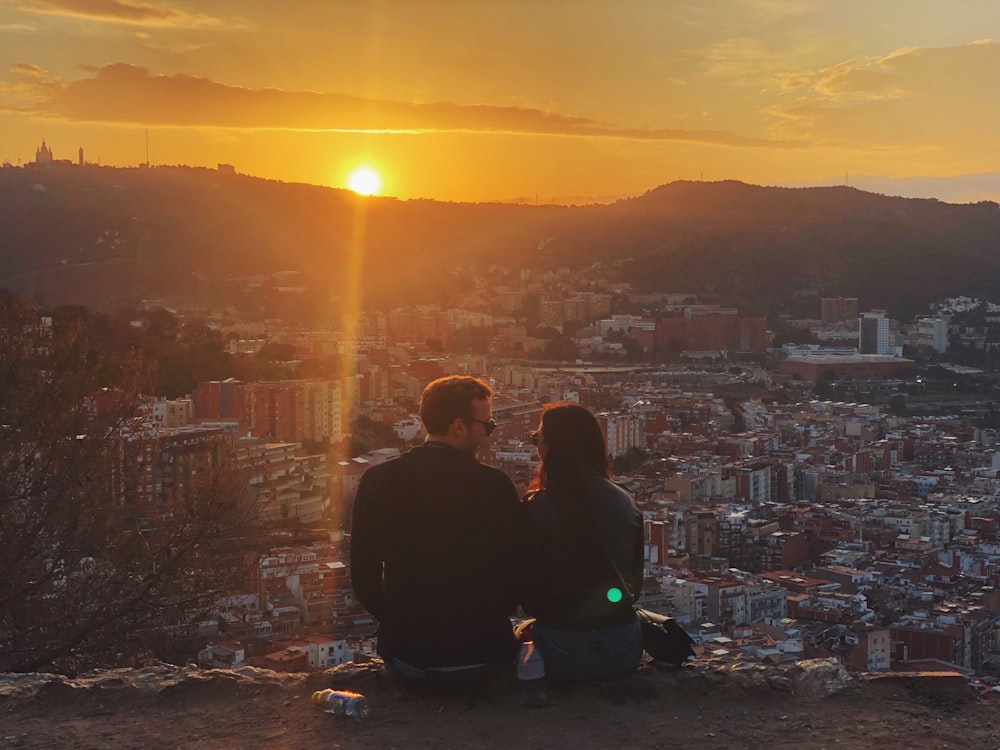 two people sitting on a hill watching the sunset