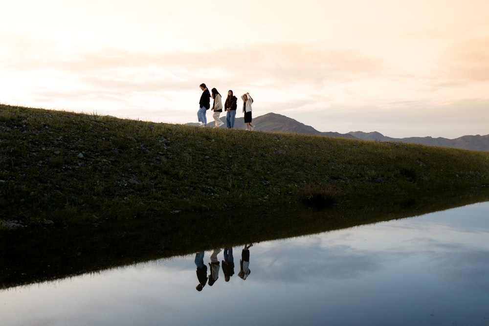 3 people standing on green grass field near lake during daytime