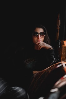 Riaan Kuppa in a thoughtful pose, seated in a dimly lit room with dark undertones and silver accents.