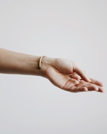 A human hand is extended with the palm facing upwards against a light, neutral background. The wrist is adorned with a simple, elegant bracelet.