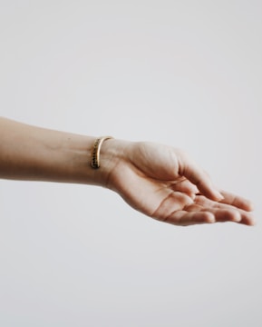 A human hand is extended with the palm facing upwards against a light, neutral background. The wrist is adorned with a simple, elegant bracelet.