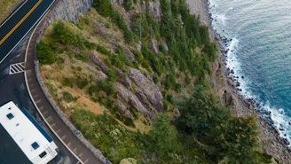 A campervan driving along a winding coastal road with cliffs and the sea in the background.