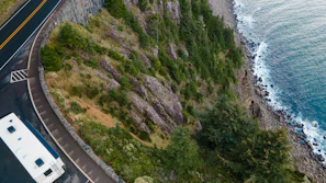 A campervan driving along a winding coastal road with cliffs and sea.