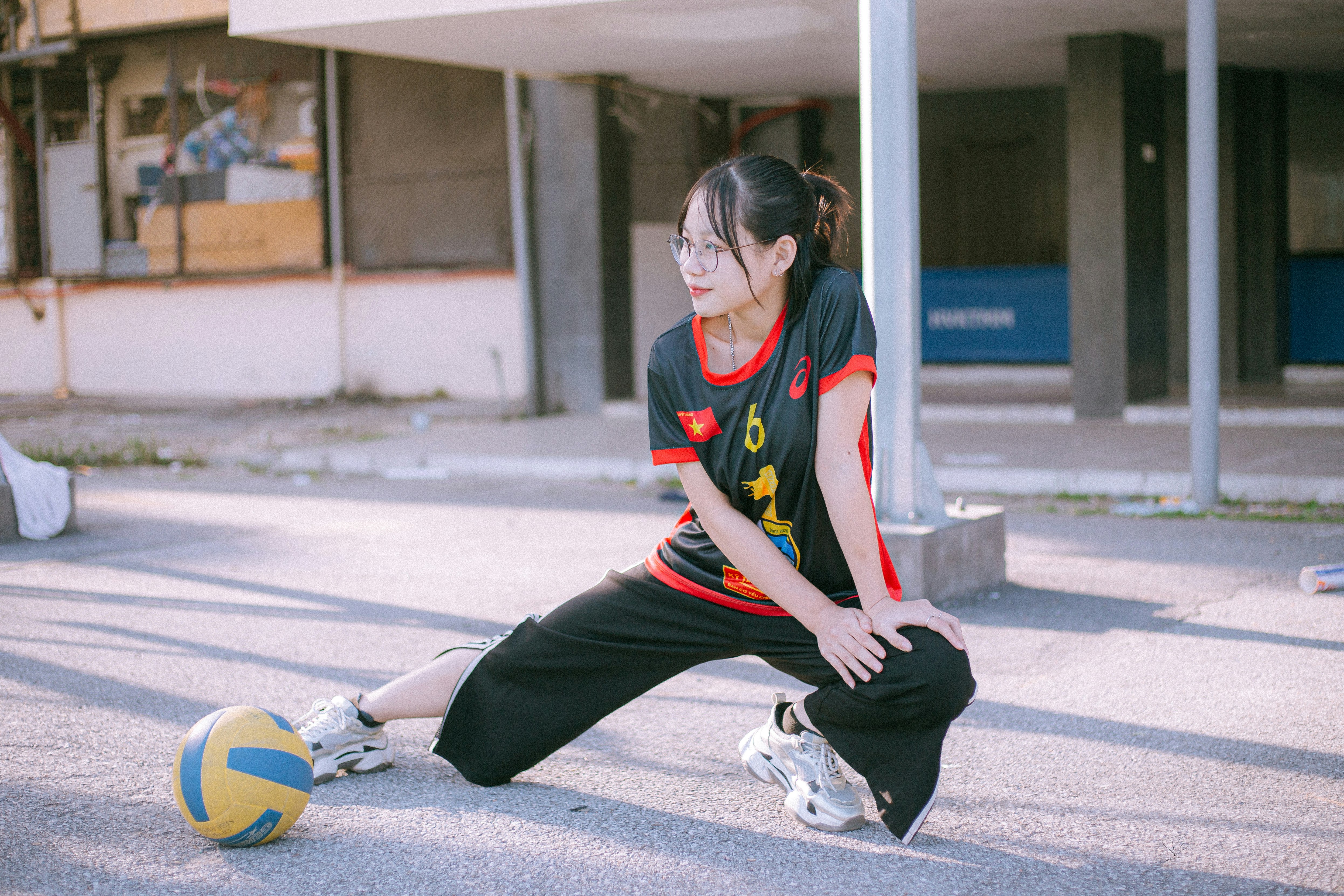 woman in black and red nike shirt and black pants sitting on gray concrete floor