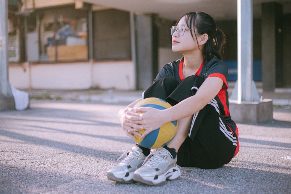 woman in black and red shirt and black pants sitting on gray concrete floor