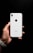 A hand holding a white smartphone with a visible brand logo and camera on the back. The background is a solid black, enhancing the contrast with the phone.