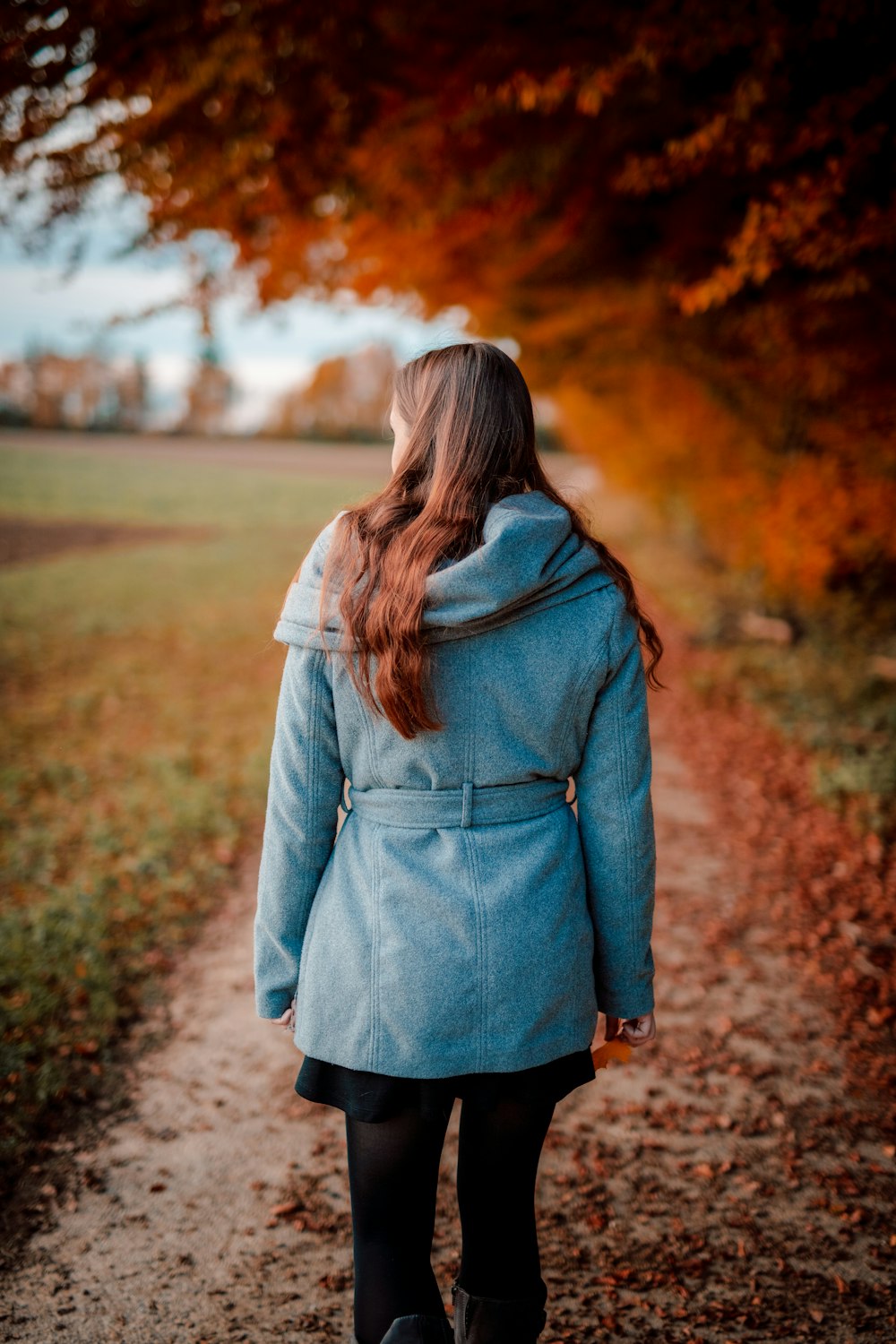 woman in gray coat standing on dirt road during daytime