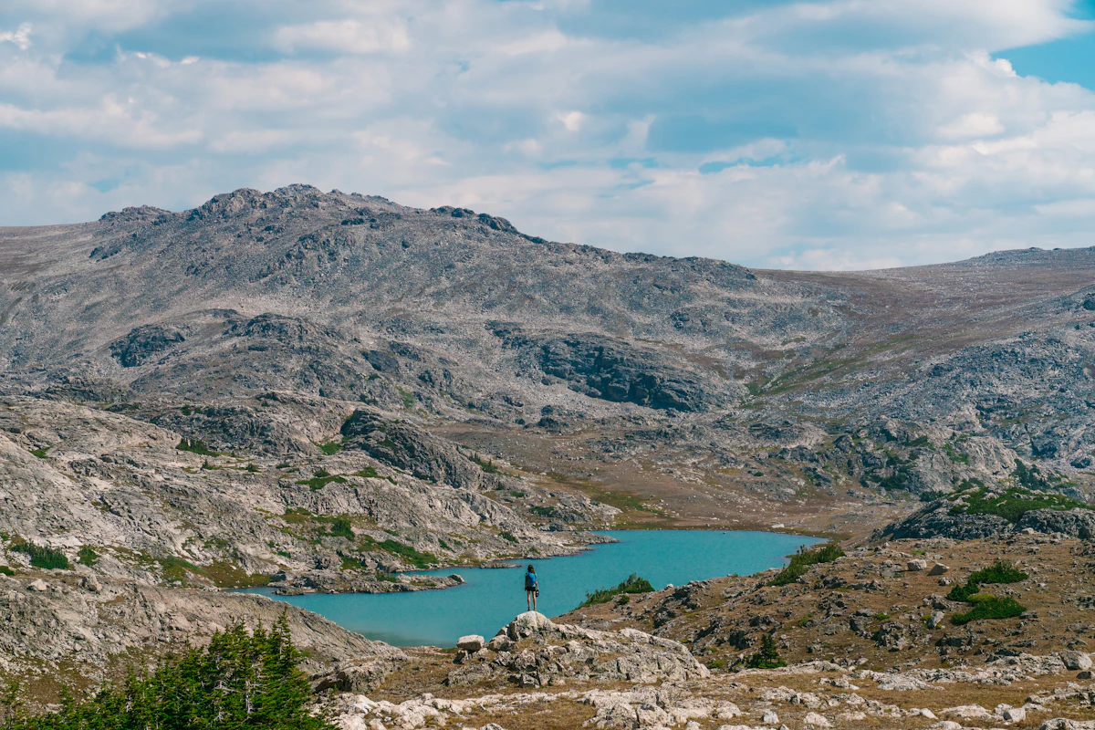 A hiker on a boulder above a turquoise alpine lake in the Bighorn Mountains, with bare granite slopes behind