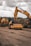 Heavy construction machinery, including a large excavator and a bulldozer, are operating on a dirt construction site. The ground shows tracks from the machinery, and the sky above is overcast with clouds.