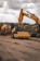 Heavy construction machinery, including a large excavator and a bulldozer, are operating on a dirt construction site. The ground shows tracks from the machinery, and the sky above is overcast with clouds.