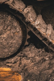 A close-up view of a bulldozer track partially coated in mud and dirt. The image highlights the intricate details of the metal links and gears, emphasizing the heavy-duty construction and rugged texture.