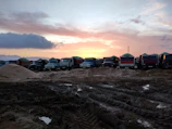 Heavy-duty trucks and equipment lined up at a busy infrastructure project site during sunrise.