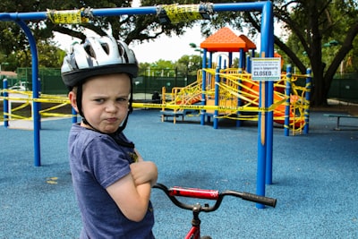 boy in blue denim vest and helmet riding red bicycle angry google meet background