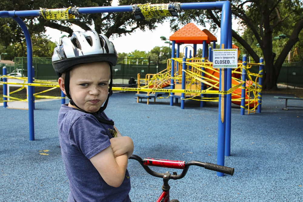 boy in blue denim vest and helmet riding red bicycle