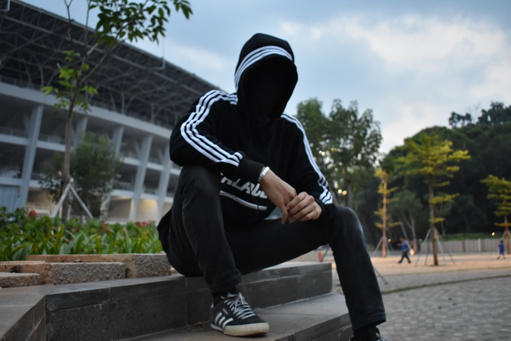 man in black and white hoodie and black pants sitting on concrete bench during daytime