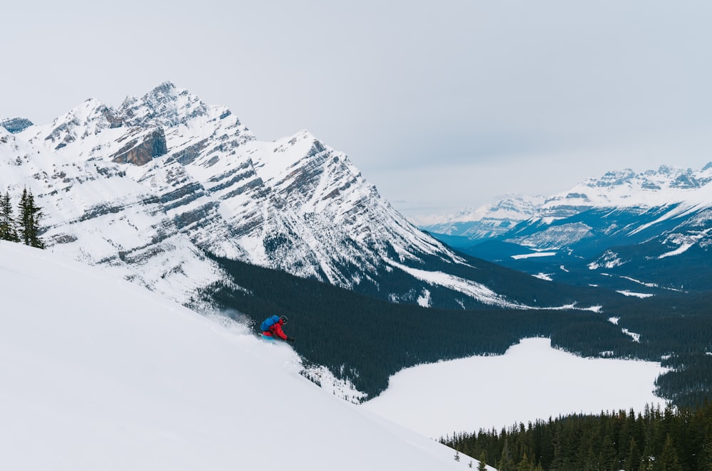 person in red jacket and black pants standing on snow covered ground near snow covered mountain