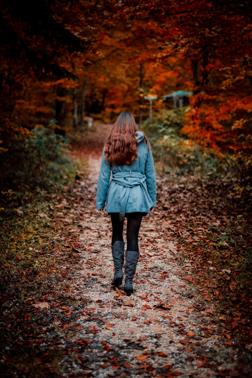 woman in gray coat walking on brown dried leaves on pathway