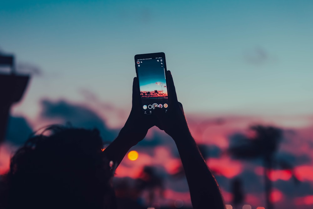 Person mit schwarzem Smartphone beim Fotografieren des Sonnenuntergangs